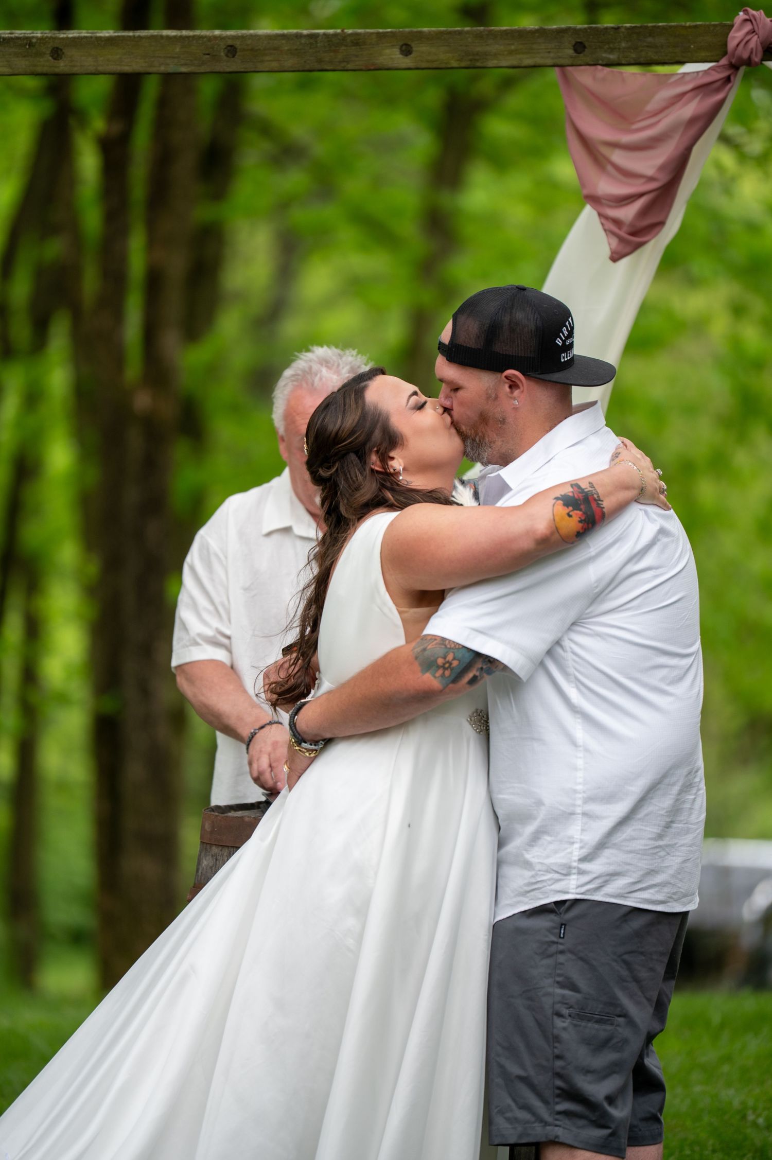 Bride and groom sharing their first kiss at an outdoor woodland wedding ceremony.