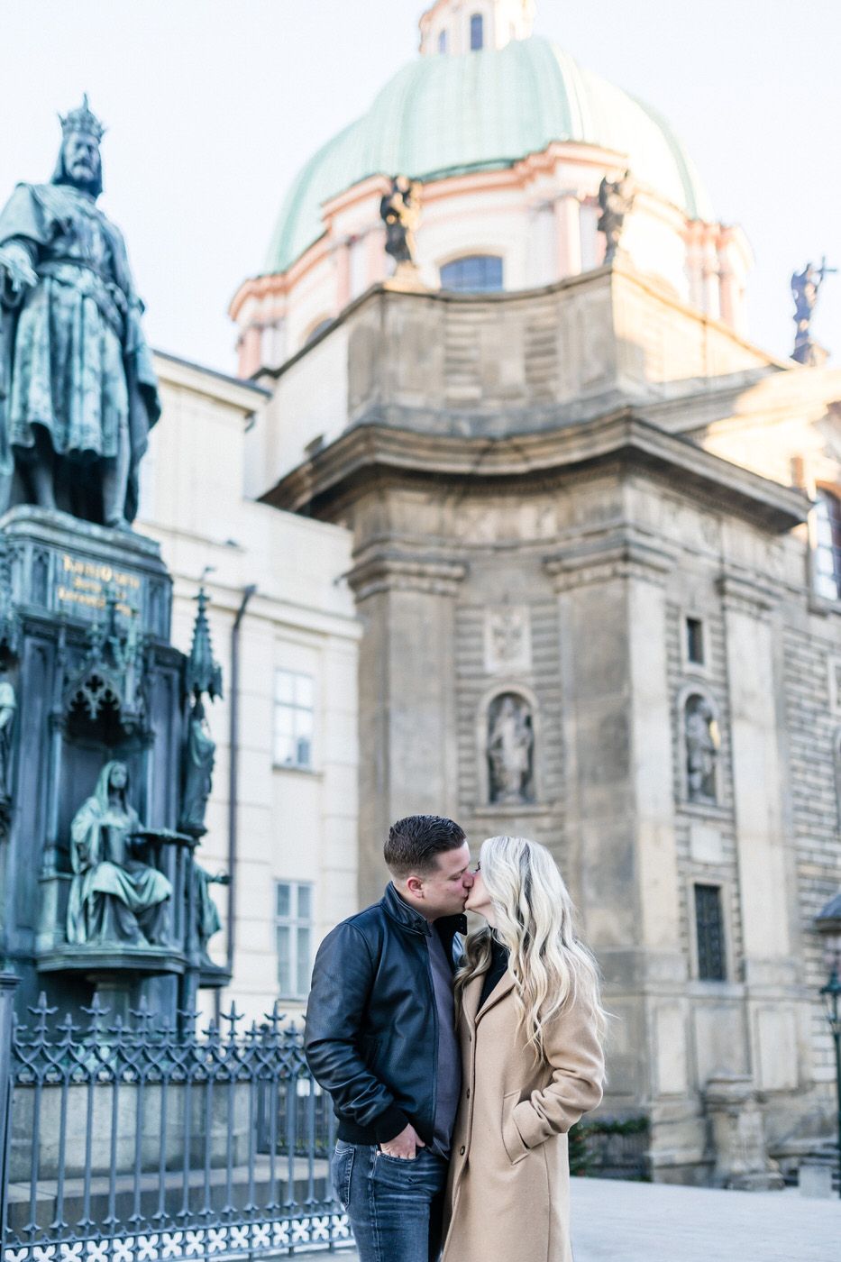 Couple sharing intimate moment in front of historic Prague church and statues.