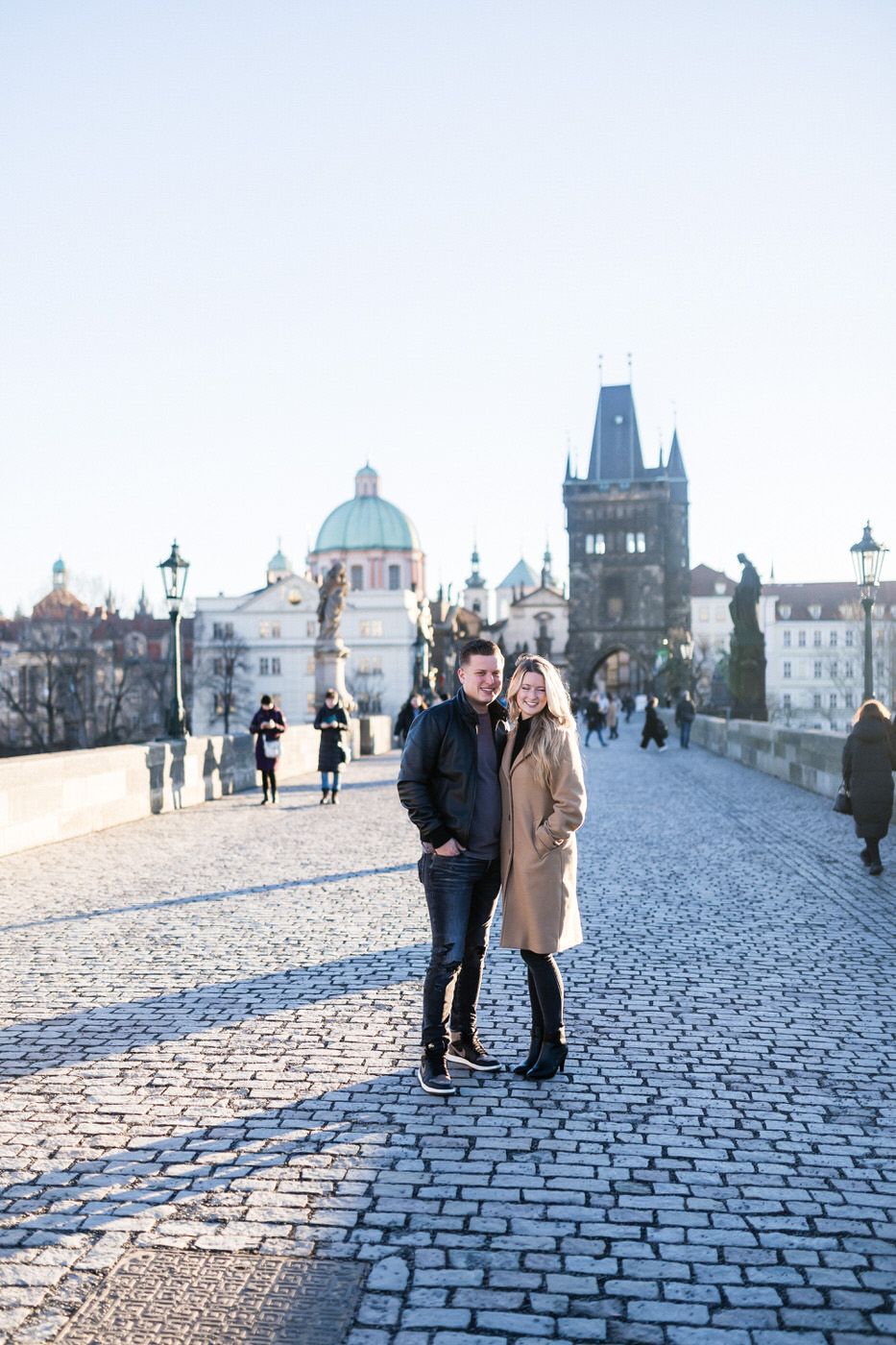 Couple posing on Charles Bridge with Prague's iconic architecture in background.