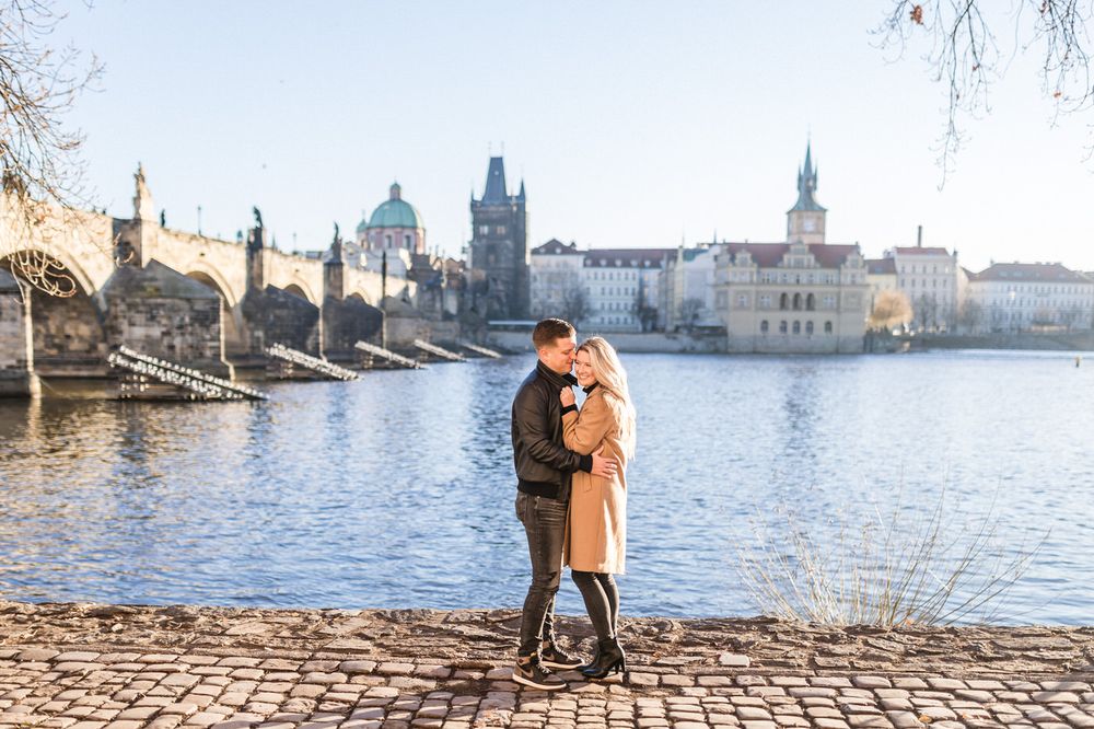 Romantic moment by Vltava River with Prague's historic Charles Bridge in background.