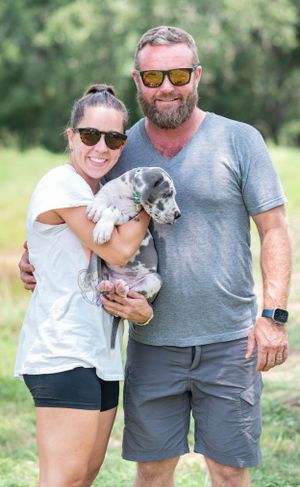 Smiling couple outdoors holding a cute gray and white Great Dane puppy together.