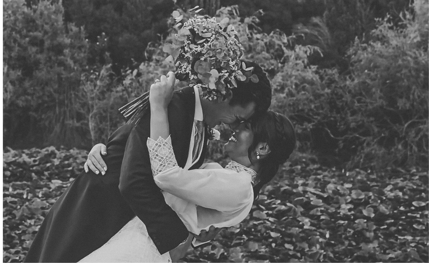 Newlyweds share an intimate moment while walking through a scenic field during sunset.