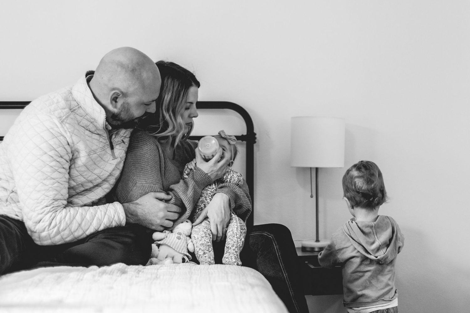 Black and white photo of a tender family moment in a bedroom.