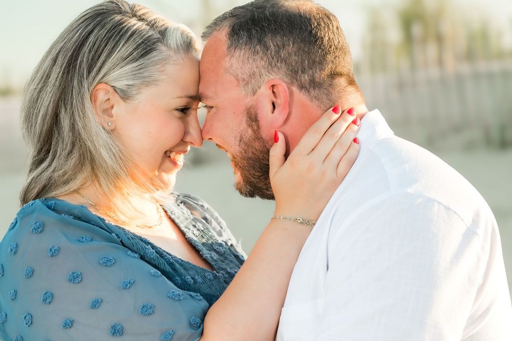 Couple sharing a romantic forehead touch on the beach, woman smiling with hands on mans face, golden hour light.