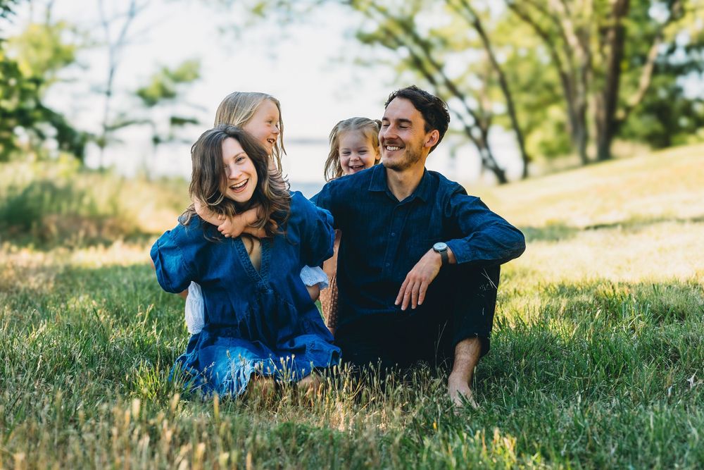 Happy family of four sitting together on green grass in a sunny outdoor park setting.
