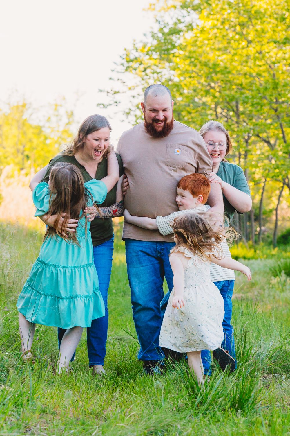 Happy family of five laughing together outdoors in a green meadow on a sunny day.