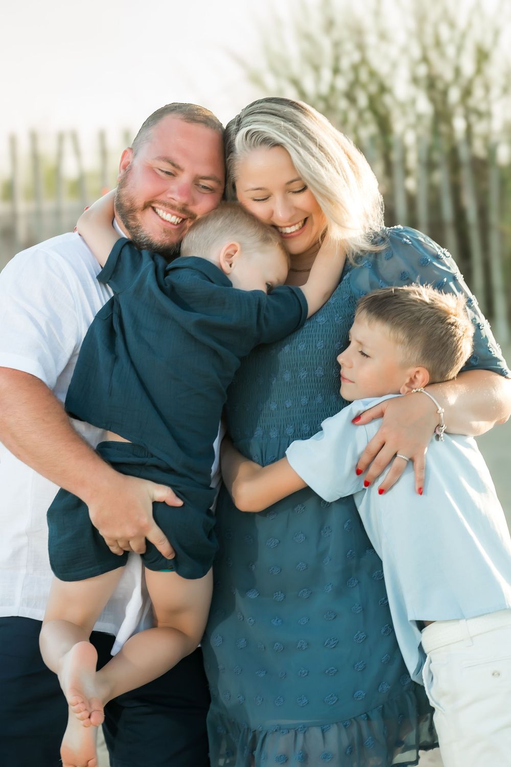 Happy family of four sharing a warm group hug outdoors, with parents smiling and two young boys embracing their mother.