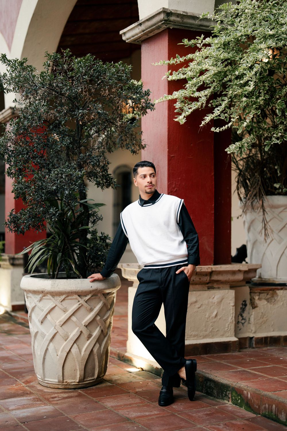 A casual portrait against a red Spanish colonial building with decorative planters.