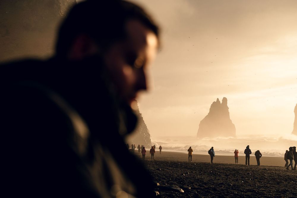 Silhouetted figures on a misty beach with dramatic rock formations in the background.