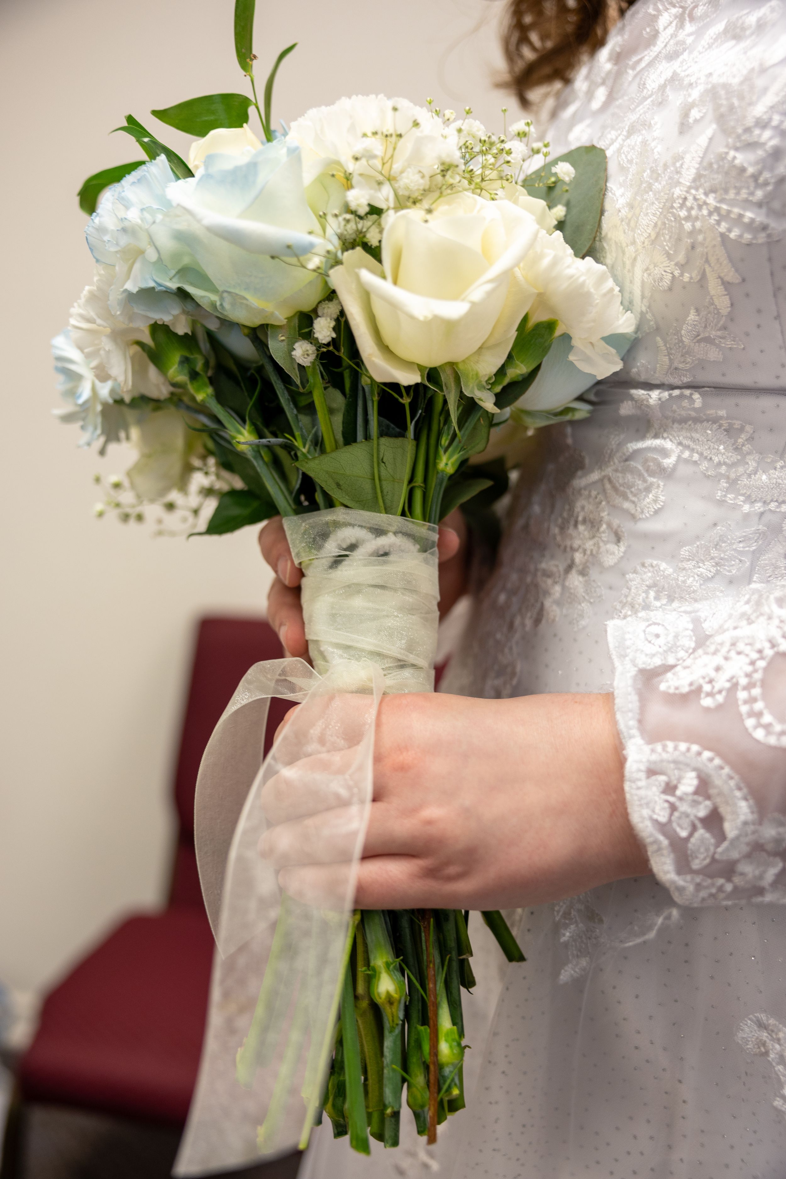 Close-up details of a white rose and lace wedding bouquet with delicate ribbon accents.