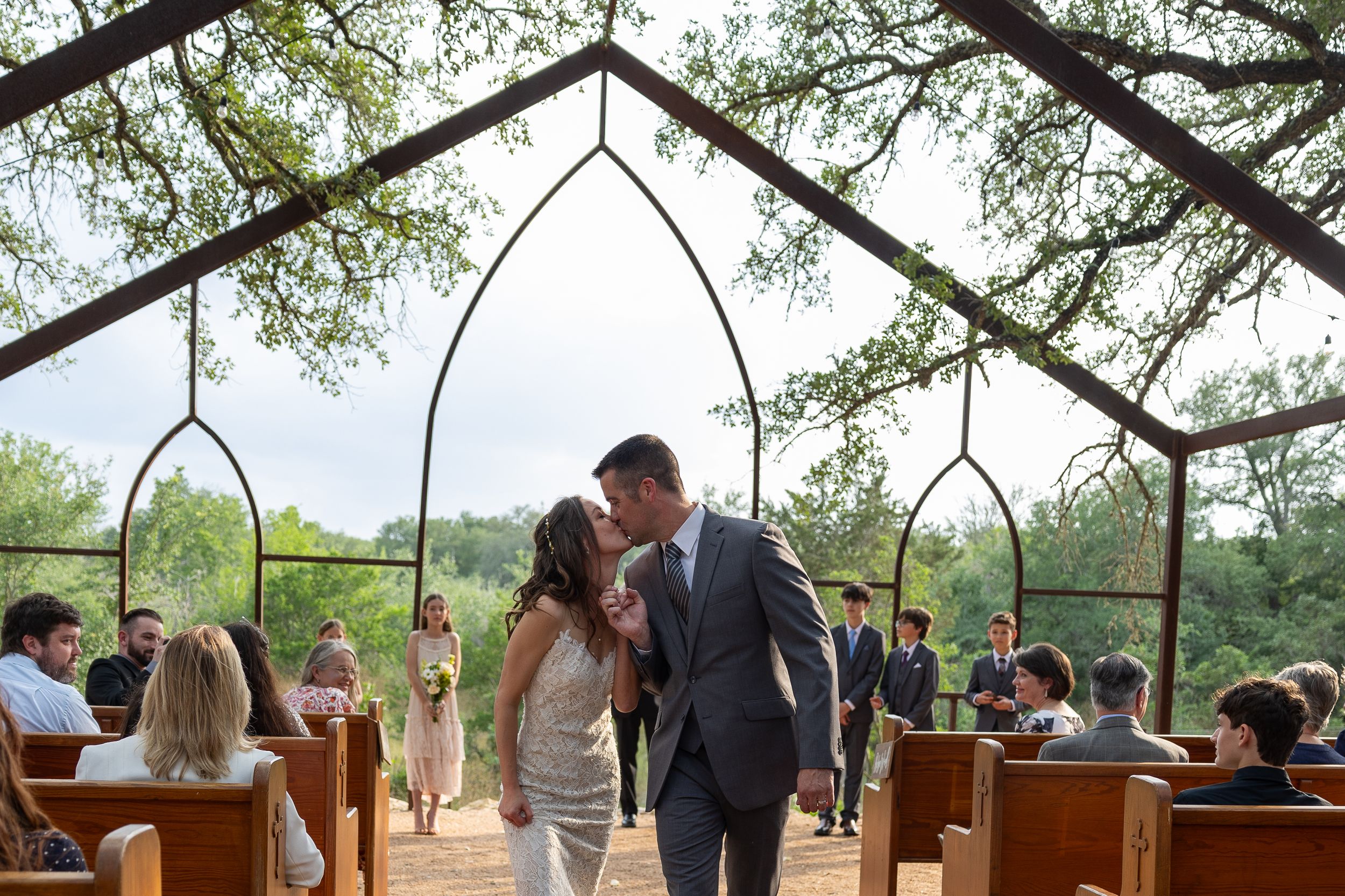 A romantic wedding ceremony moment under an outdoor pavilion with gothic-style arches.
