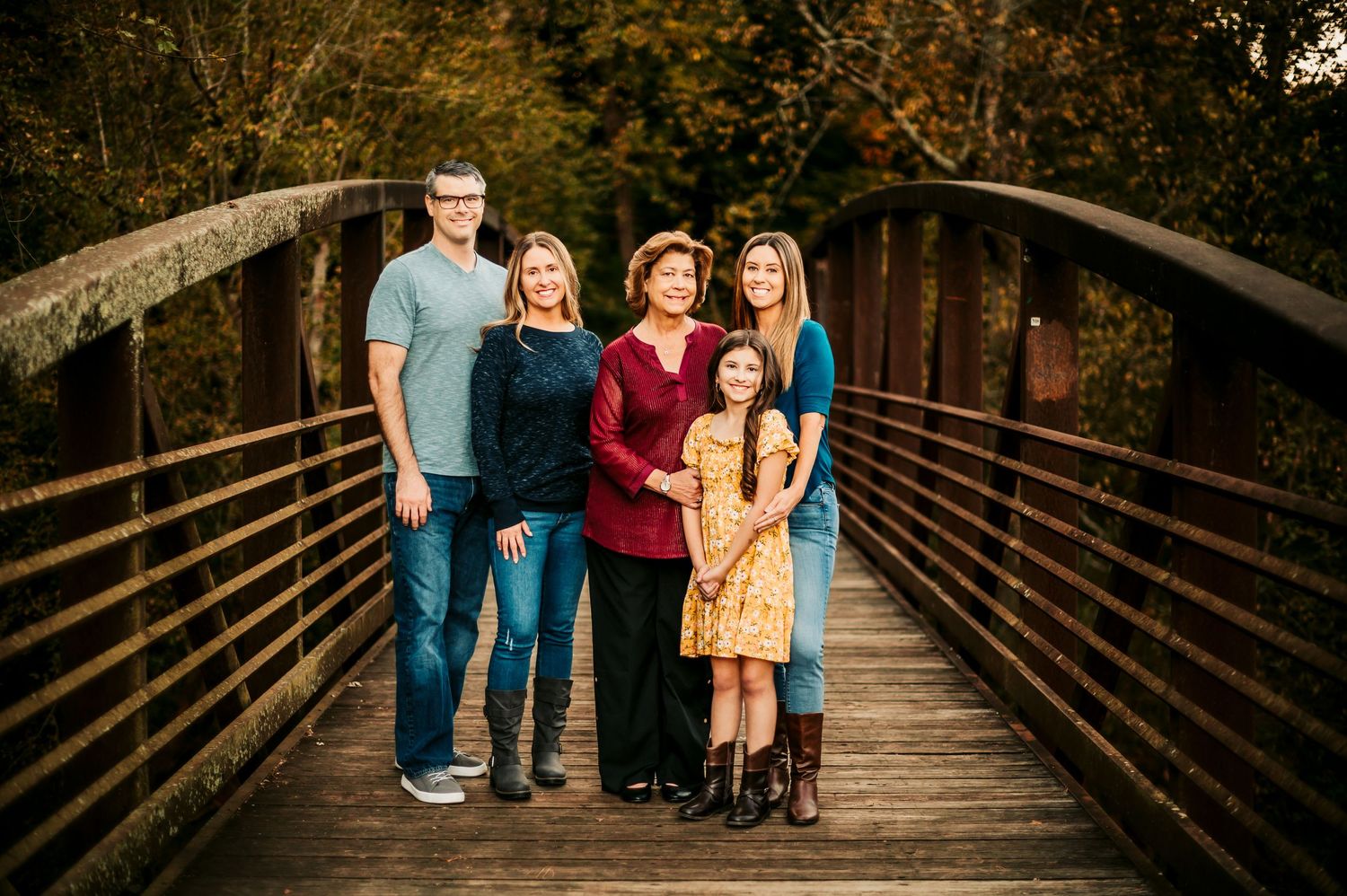 Family poses together on wooden bridge during outdoor photo session.