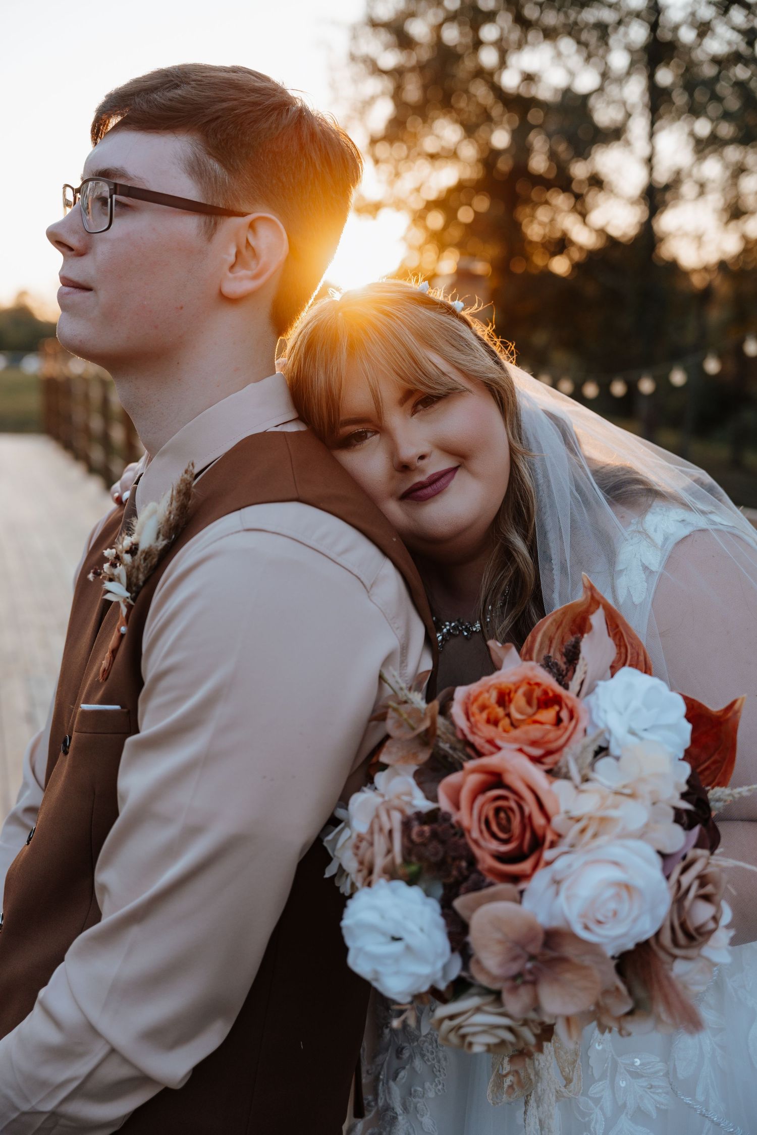 Newlyweds share an intimate moment at sunset with a bouquet of pink and white roses.