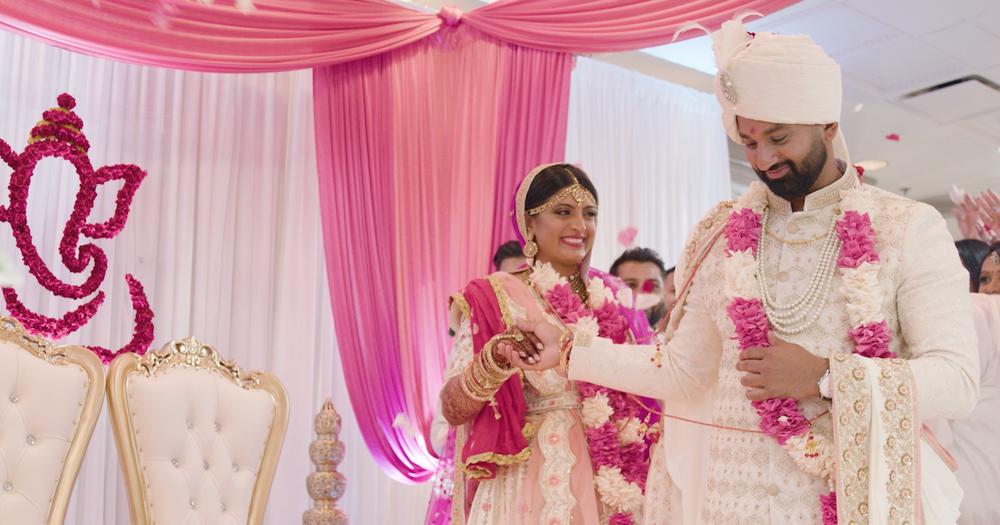 South Asian Bride and Groom Exchanging Garlands During Wedding Ceremony with Pink Drapes and Ganesha Decor