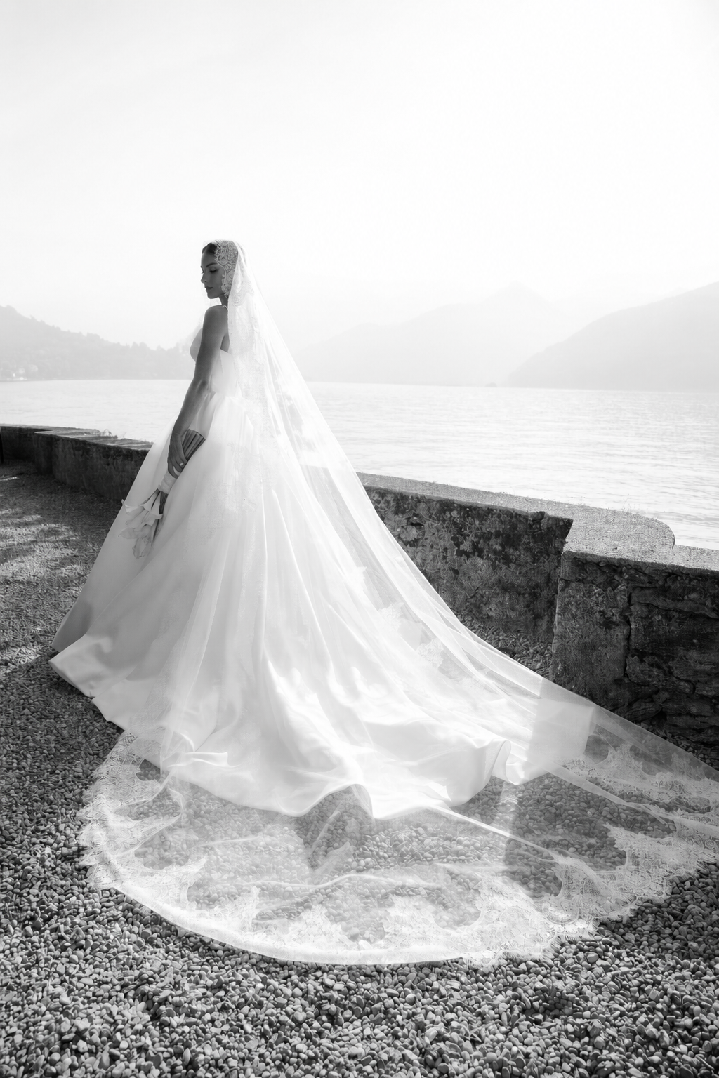 A person in a white wedding dress stands in an elegant arcade hallway with marble floors and ornate architecture.