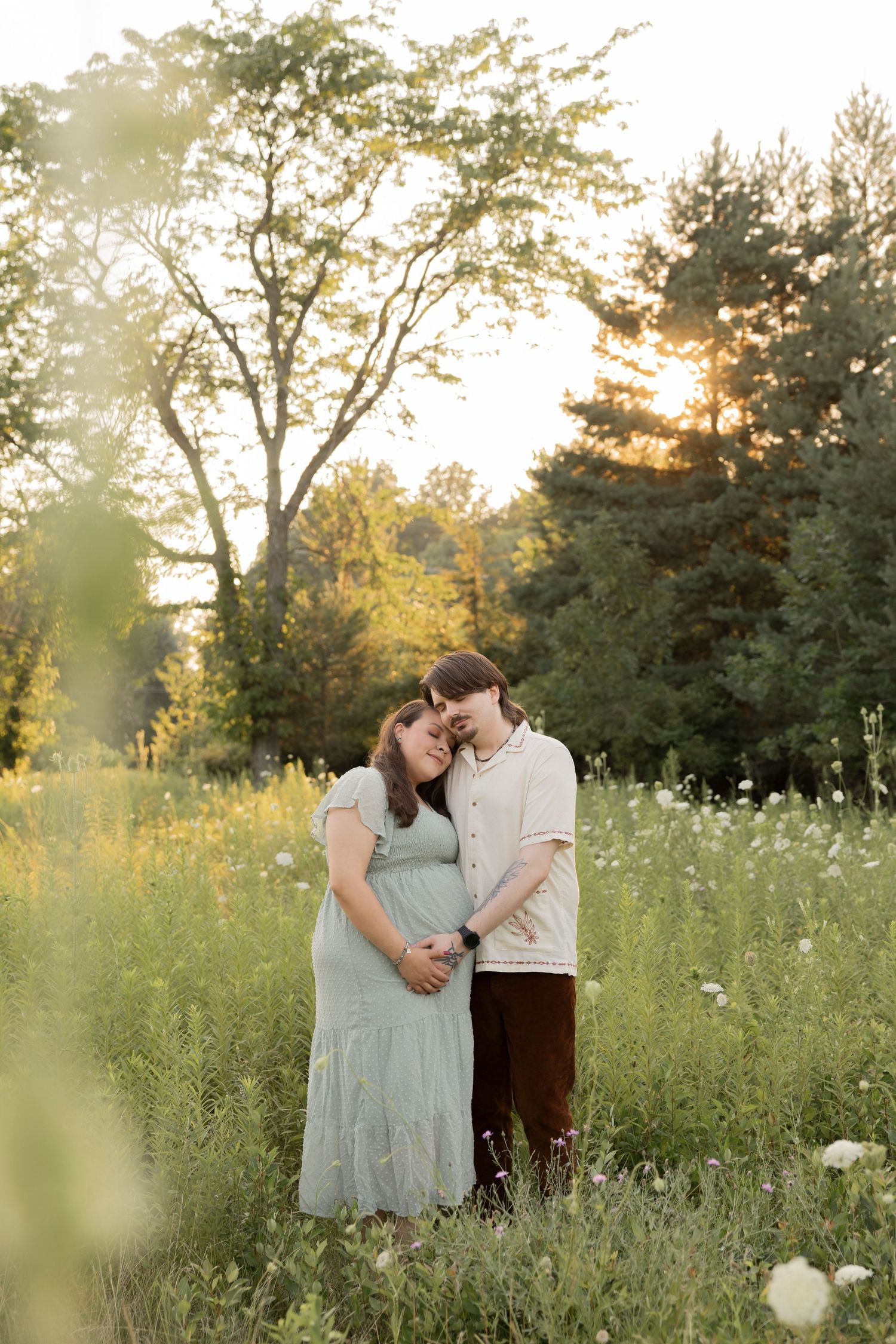 A couple in white outfits embraces while standing on a wooden boardwalk surrounded by tall grasses at sunset in west Bloomfeild Michigan