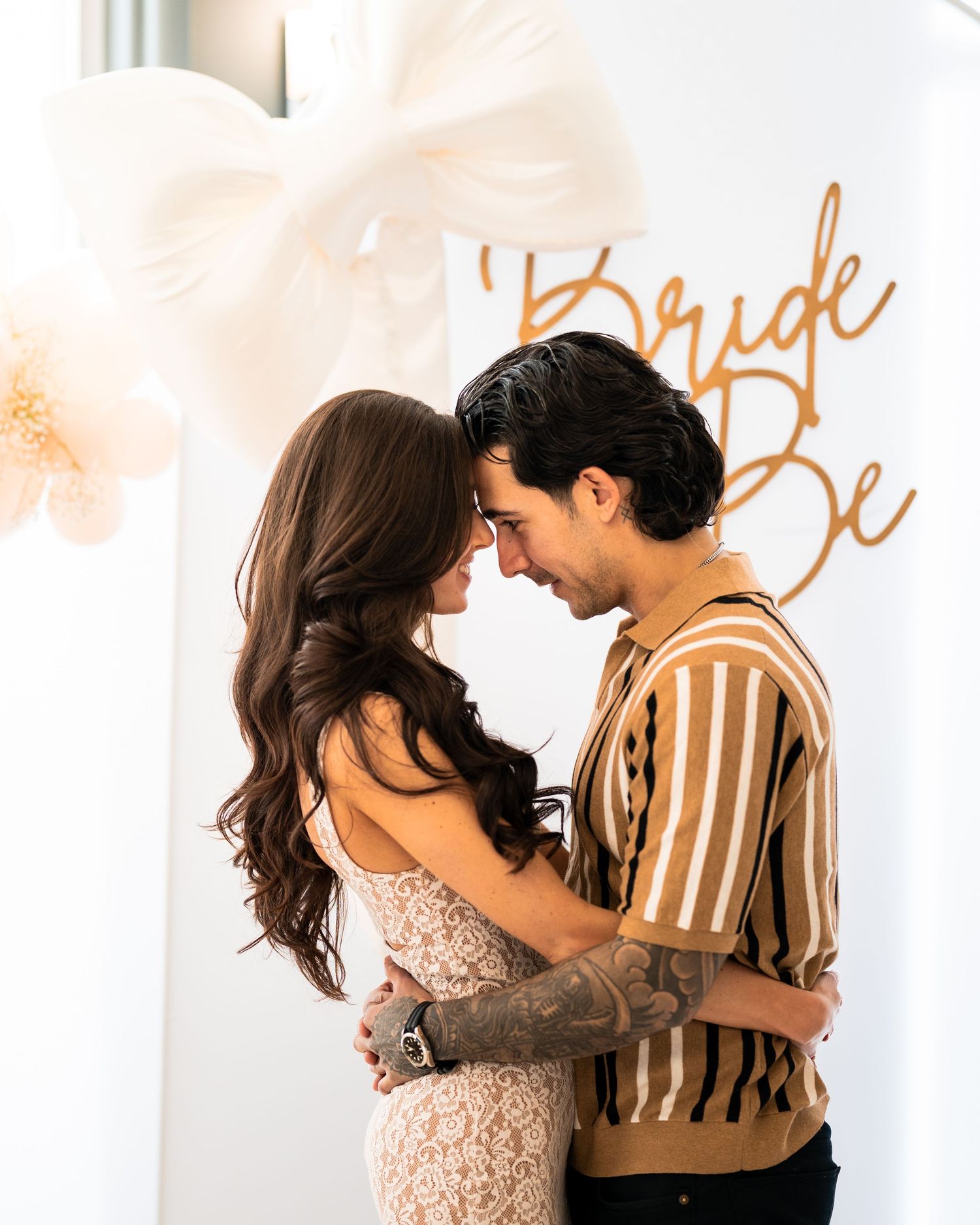 A couple shares an intimate moment against a wall with 'Bride to Be' text and balloons.