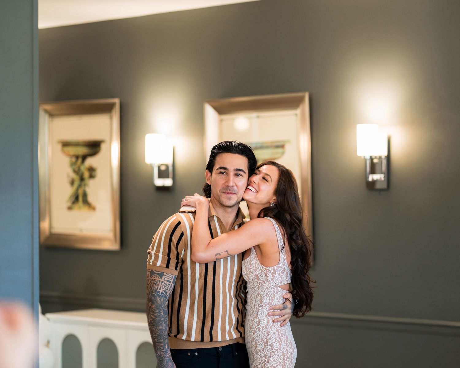 A couple shares an intimate moment in an elegant room with wall sconces.