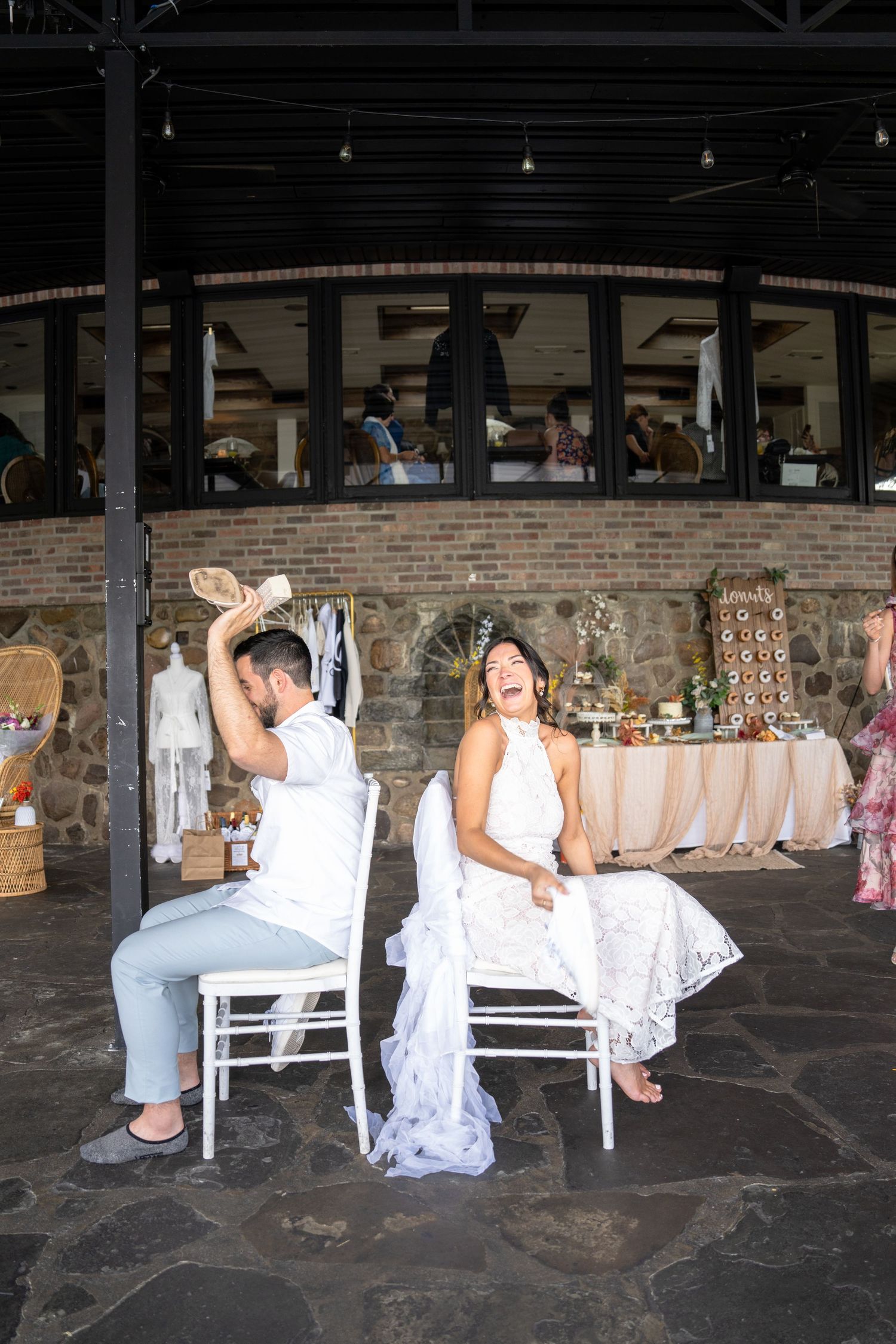 A couple plays a wedding game while seated in white chairs at an outdoor venue.