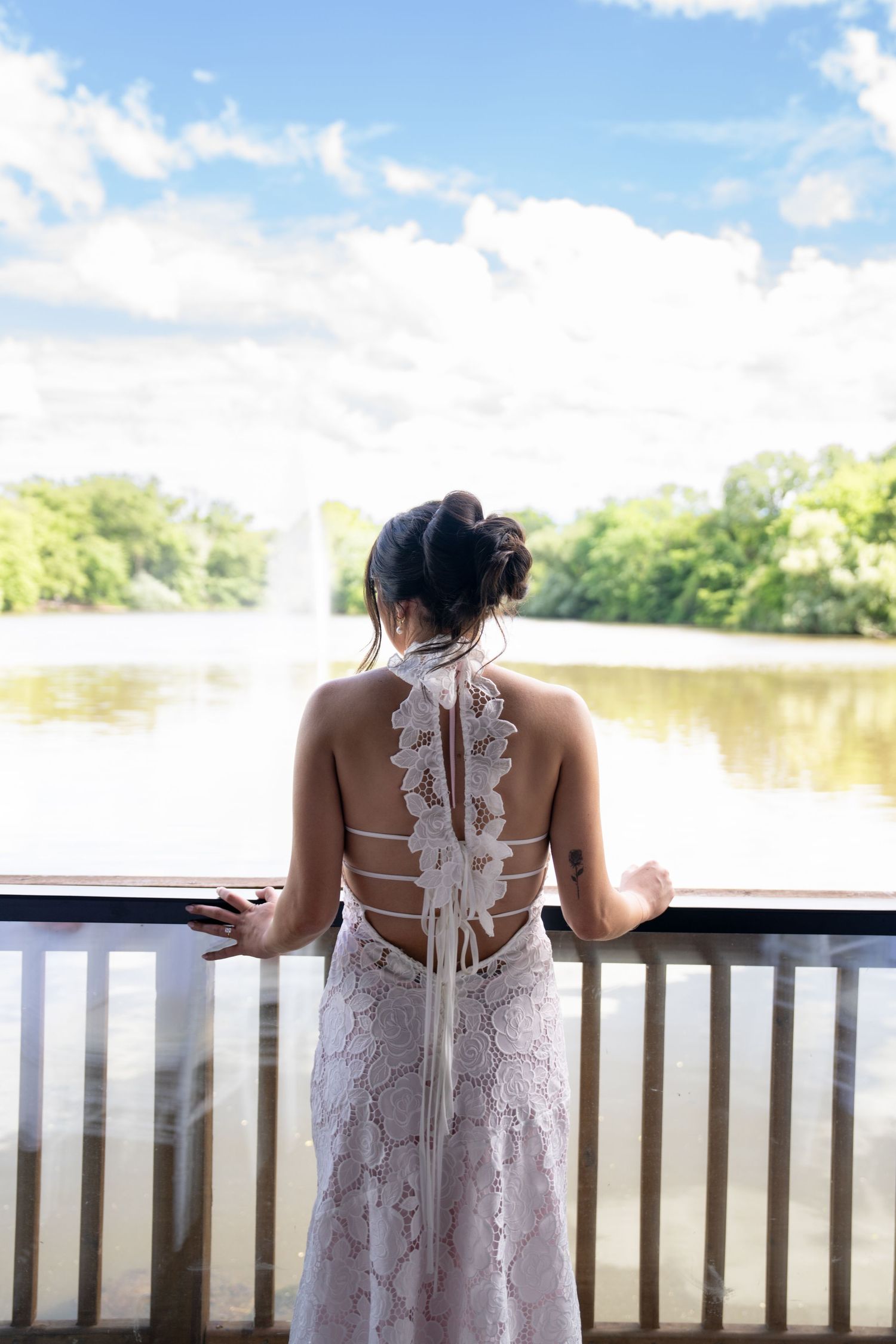 Elegant white lace dress detail shown against a waterfront deck railing on a sunny day.