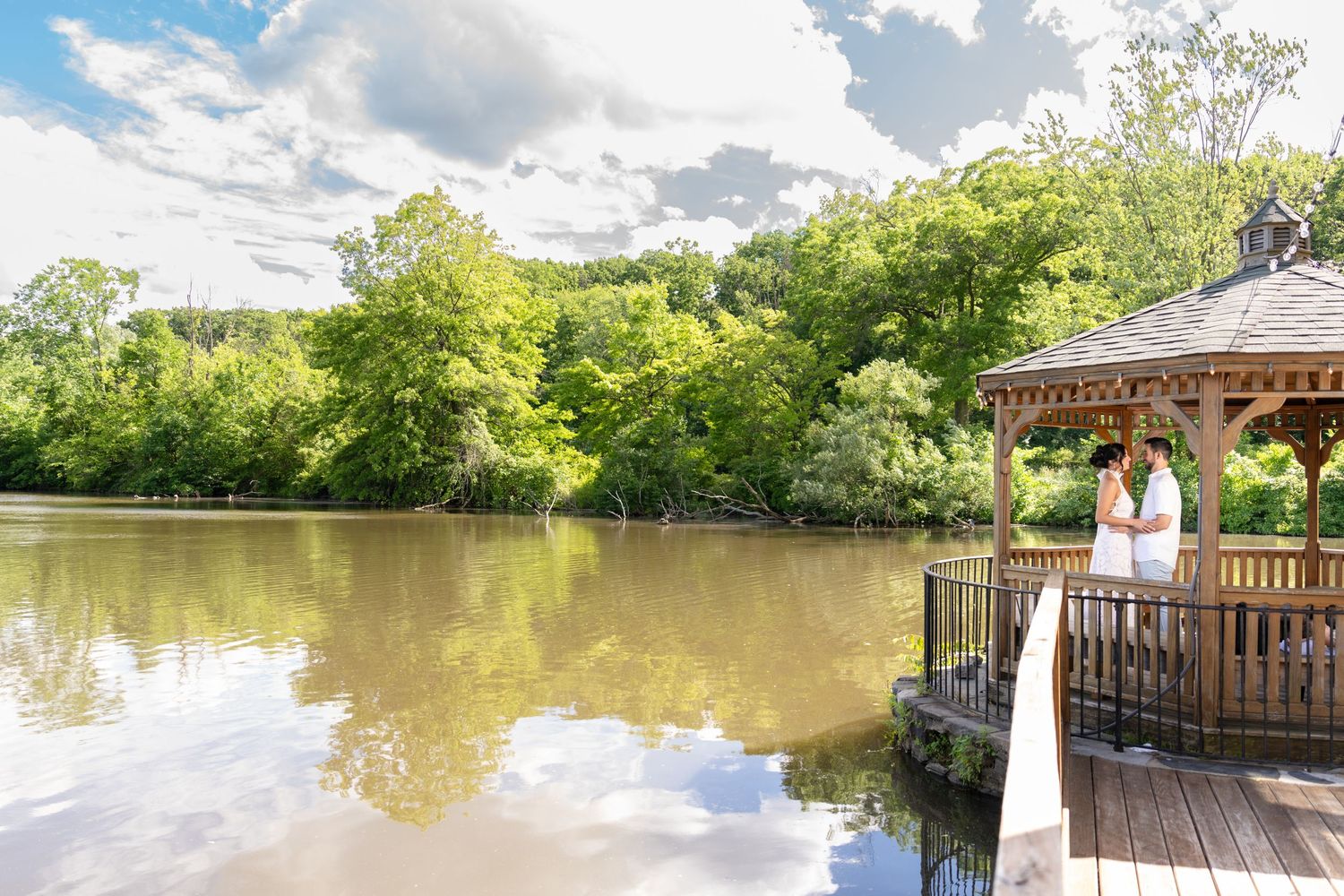 Panoramic view of a peaceful lake from a wooden deck surrounded by trees.