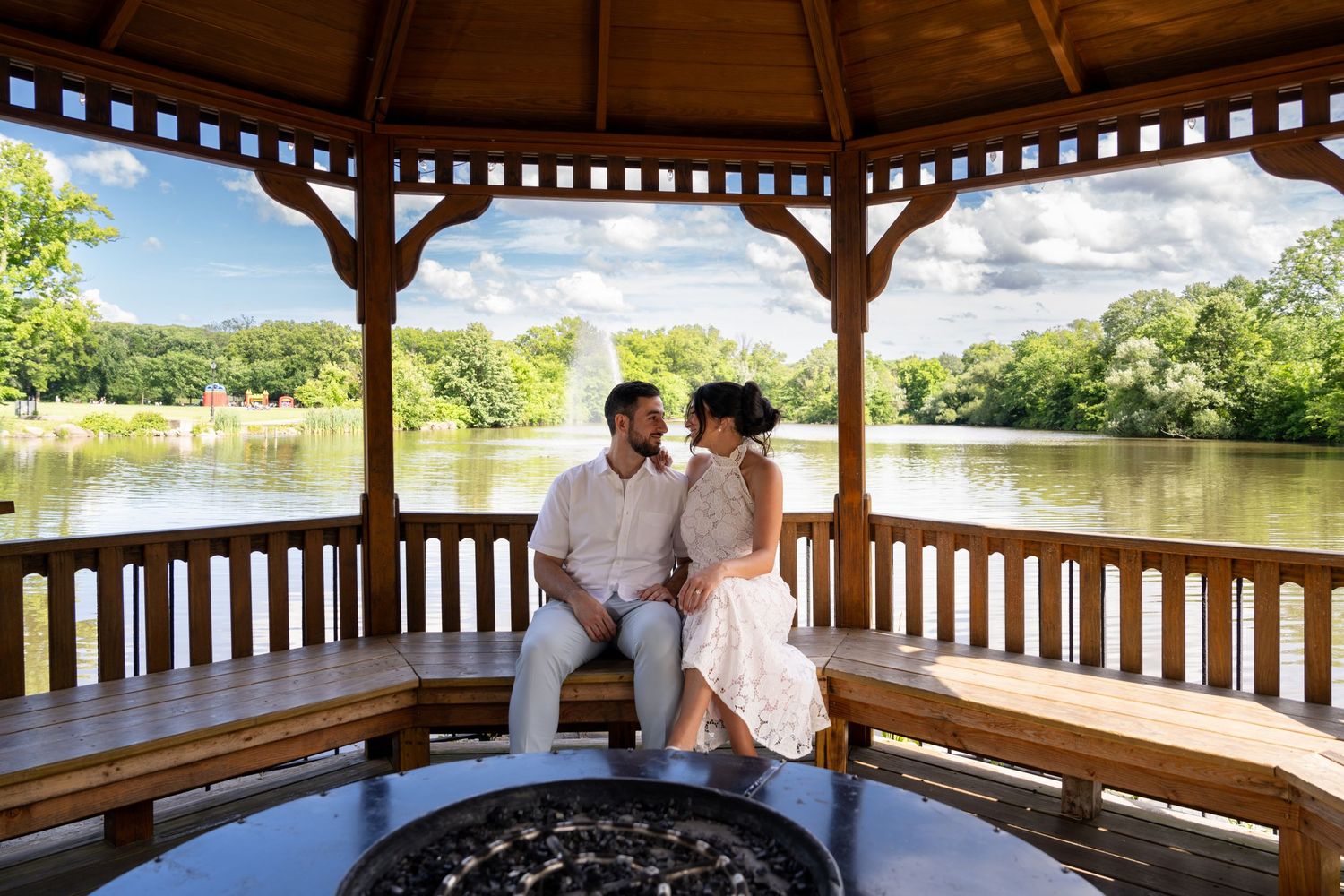 Wooden gazebo overlooking a serene lake with lush greenery in the background.