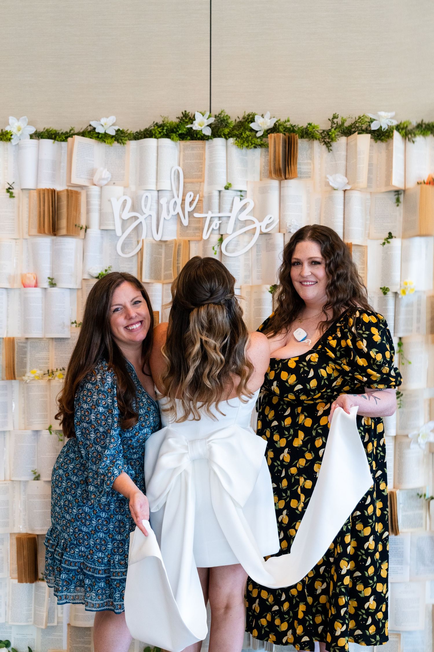 Three people posing together at a bridal celebration with a decorated book page backdrop.