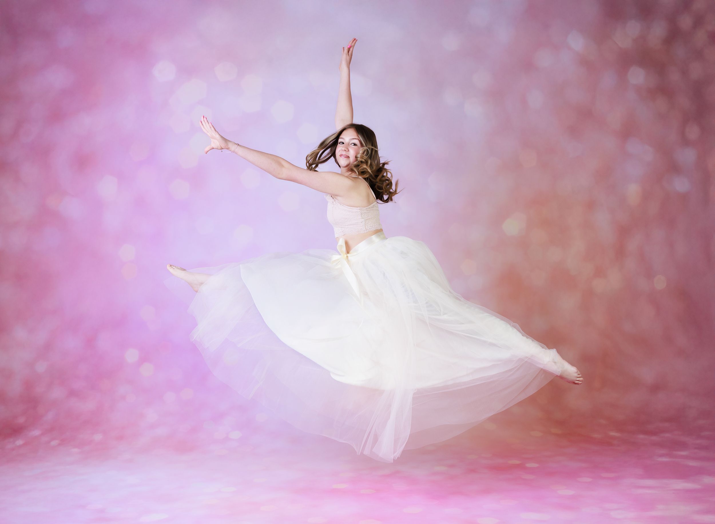 A dancer in a white flowing dress leaps gracefully against a soft pink ethereal background.