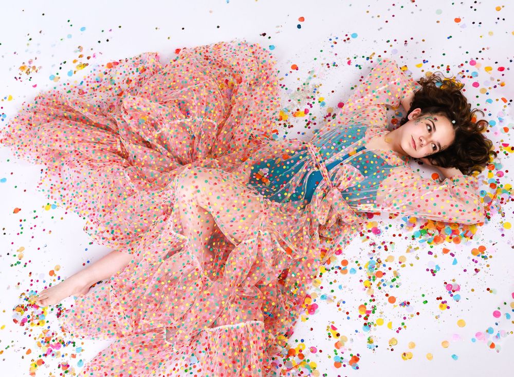 A dreamy portrait on a floor surrounded by colorful confetti with a flowing pink polka dot dress.