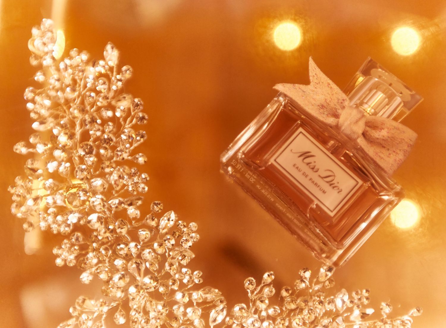 Perfume bottles and delicate white flowers photographed with golden bokeh lighting effects.