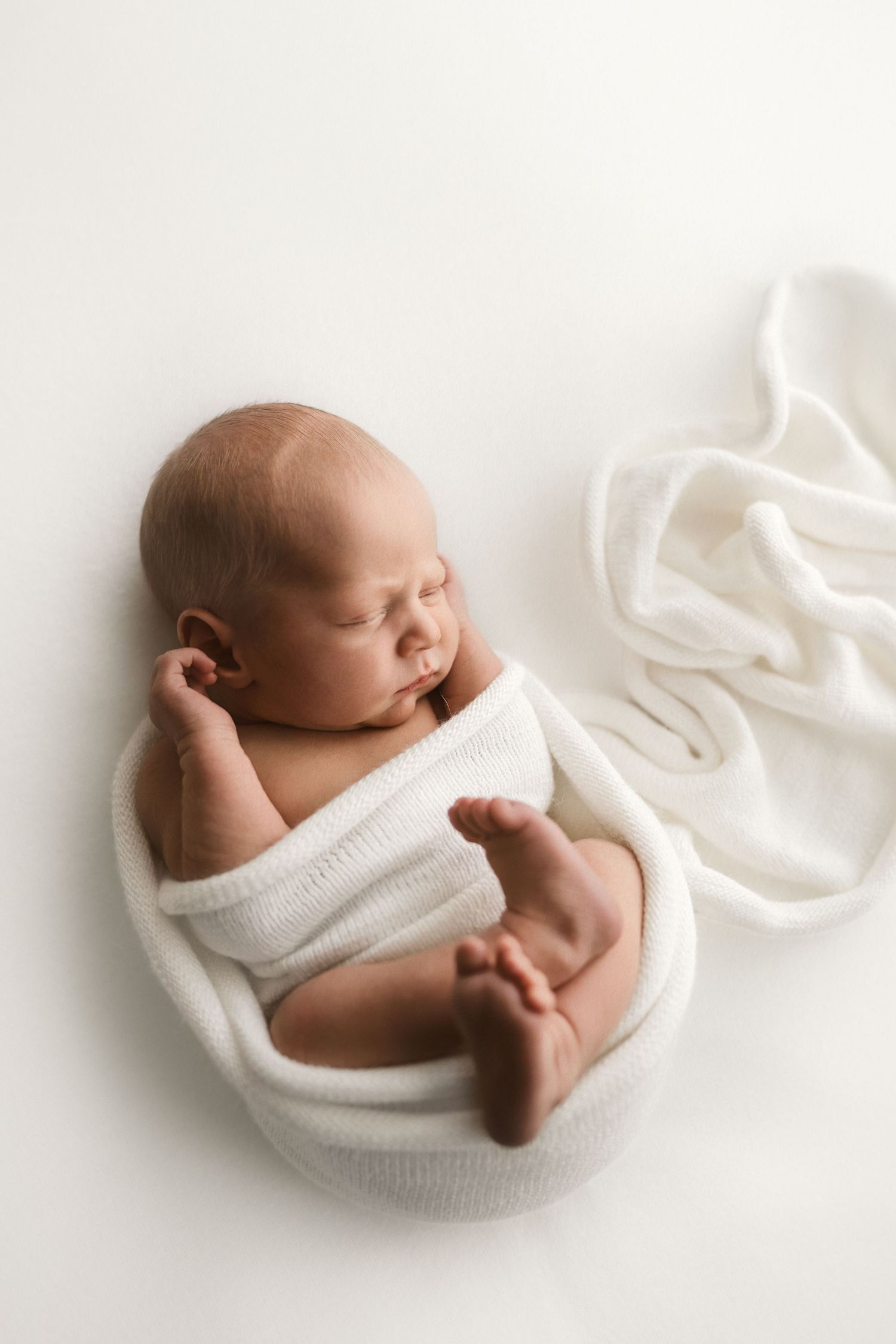 Newborn baby wrapped in white fabric held gently by tattooed hands.