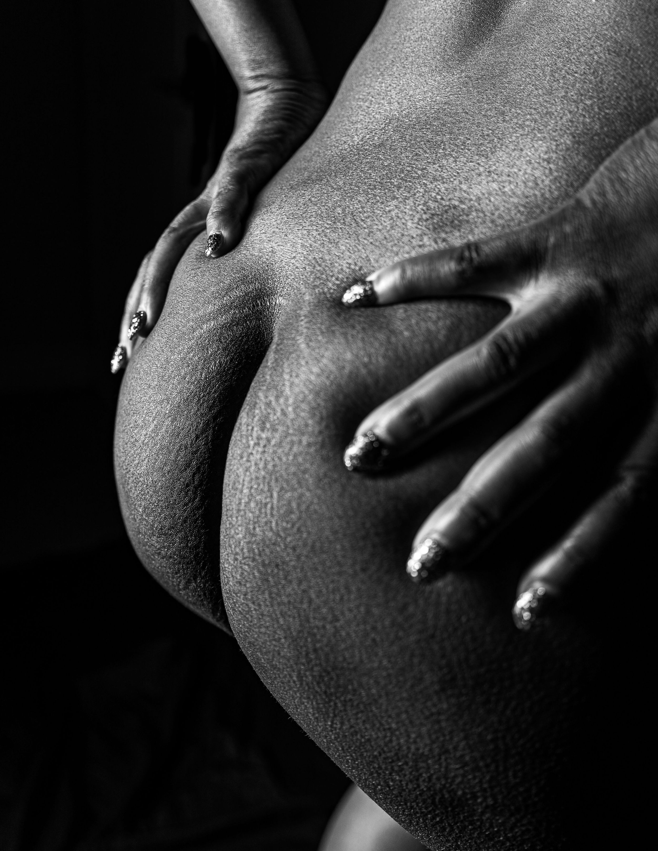 Black and white artistic photograph showing hands with long manicured nails resting on a curved dark surface in shadow.