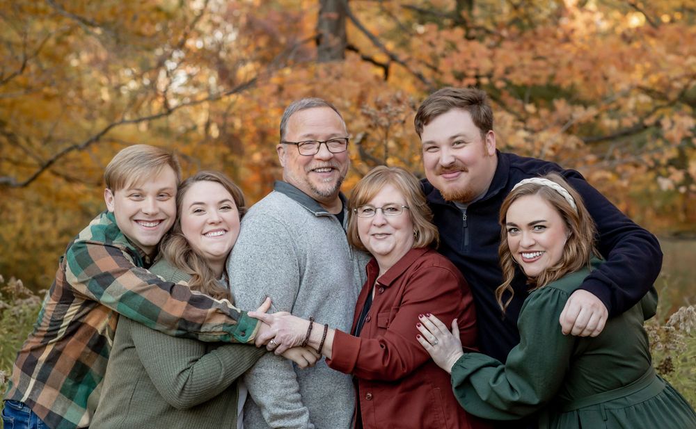 Happy family of six embracing and smiling together among colorful autumn foliage.