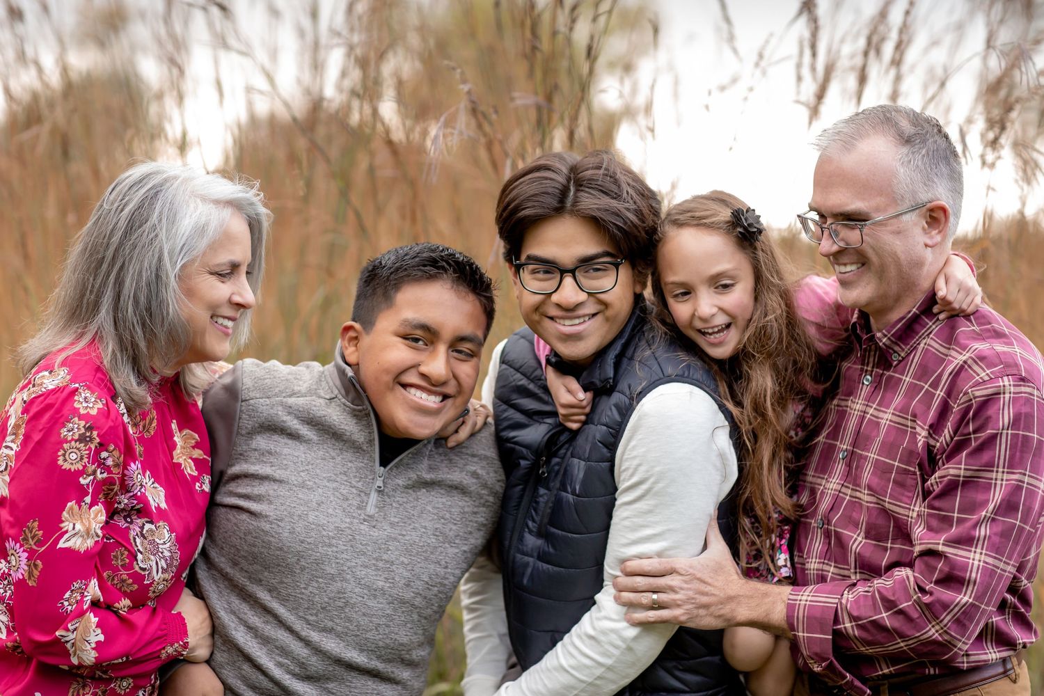 A happy family of five embraces and laughs together outdoors near a serene waterway.