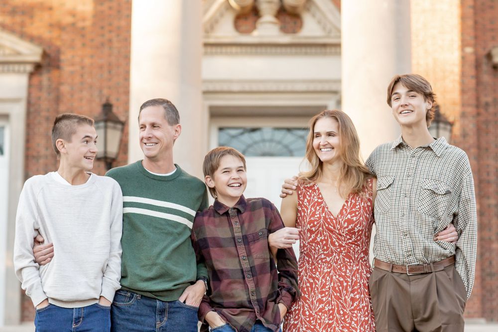 Smiling family of five posing together in front of a brick building outdoors.