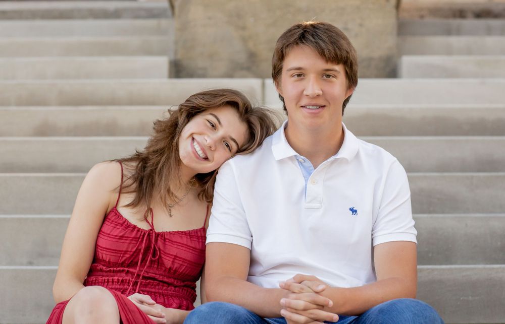 Smiling young couple sitting together on outdoor stone steps in casual attire.