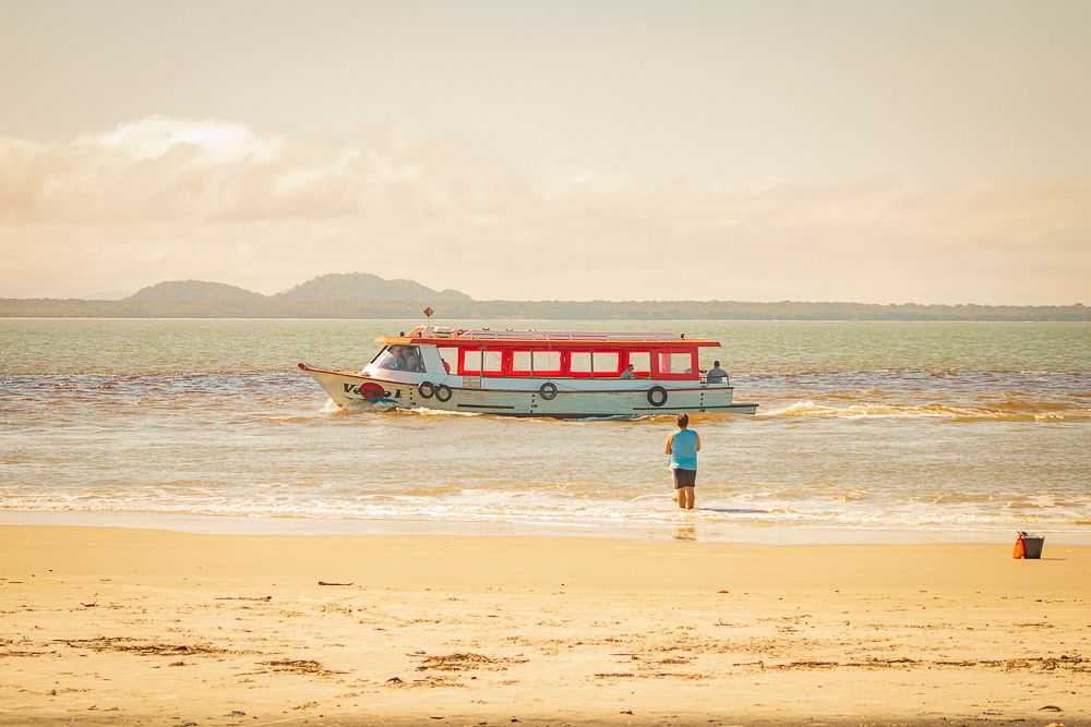 Coastal beach scene with red boat on calm sea, photographed by Piret Victoria Ribas.