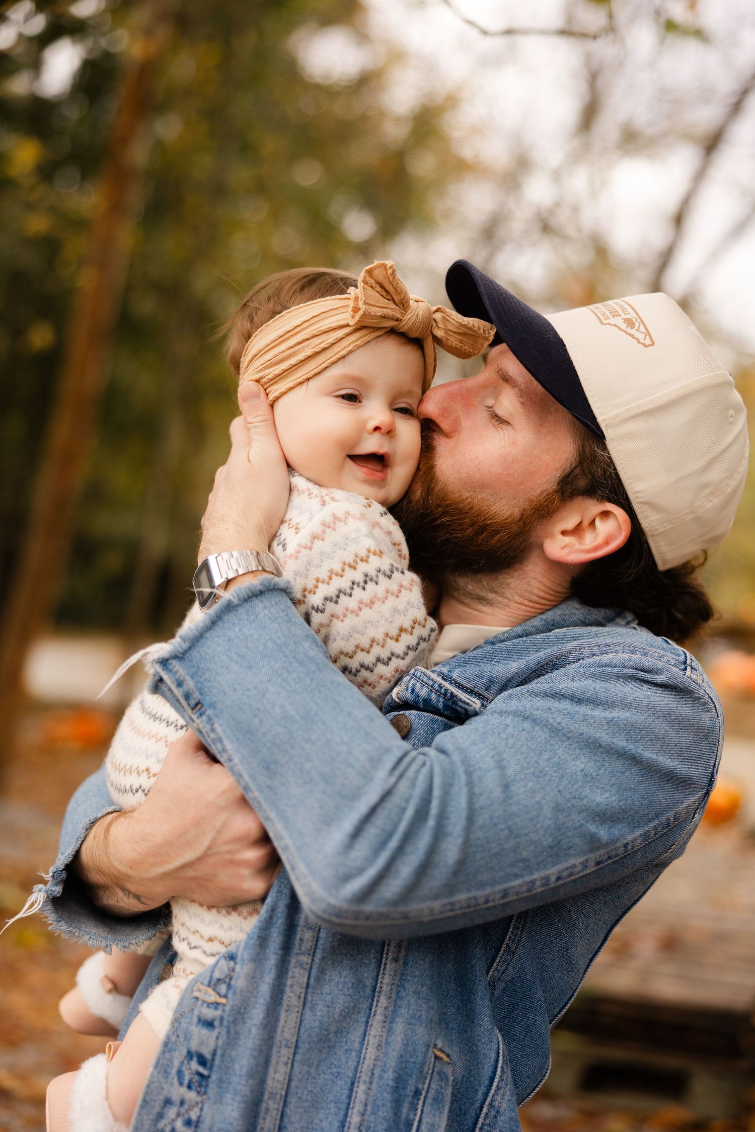A tender moment between a parent and baby in a denim jacket outdoors during autumn.