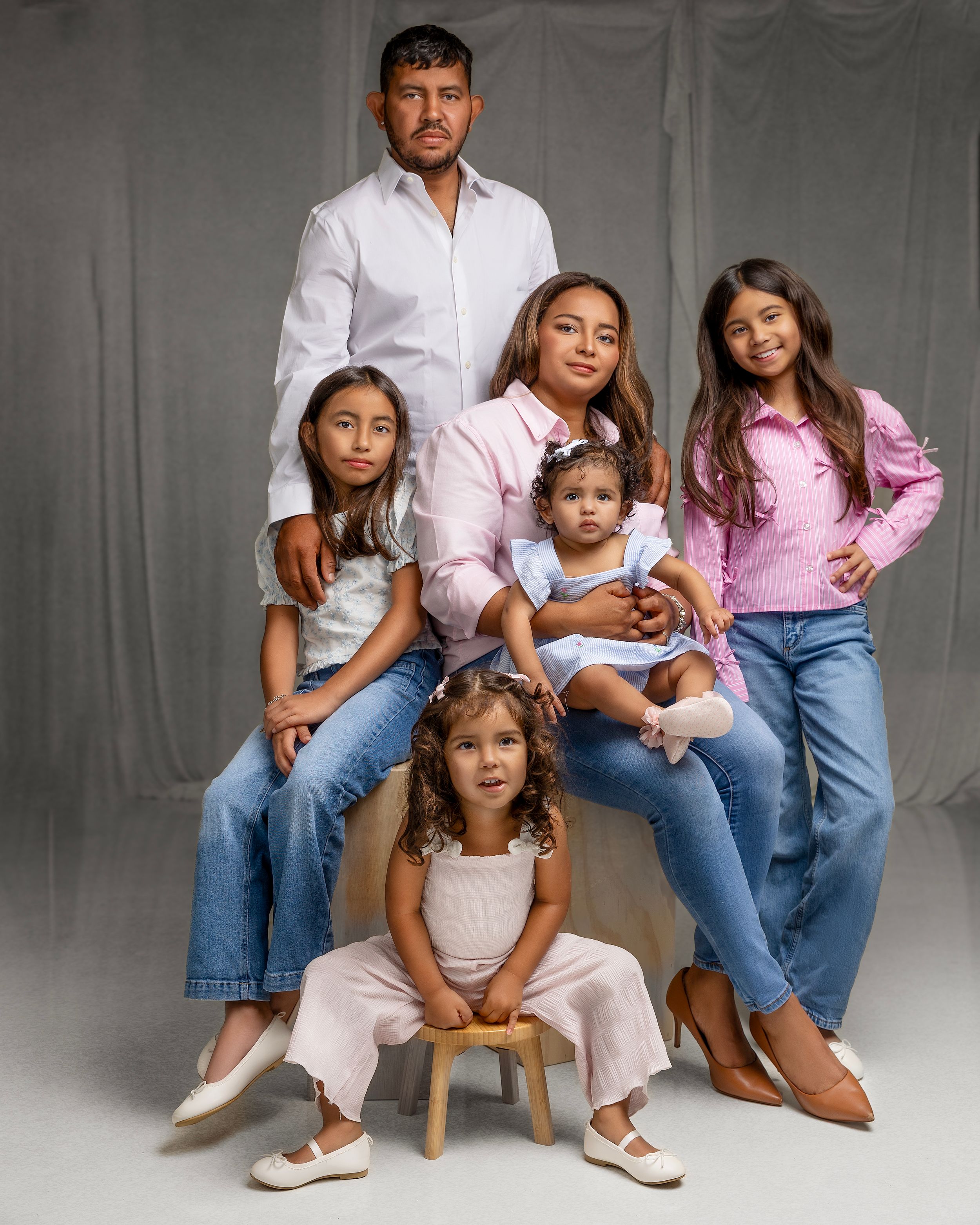 A family portrait against a gray backdrop, wearing coordinated casual outfits in white, pink and denim.