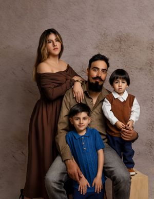 Family portrait session in brown and blue tones against a textured neutral wall.