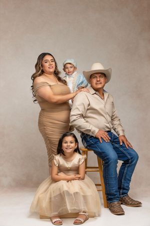 Three artistic portrait poses of a family in beige and denim sitting on wooden stools against a neutral backdrop.