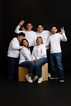 A group in matching white long sleeve tops and blue jeans pose together against a dark background.