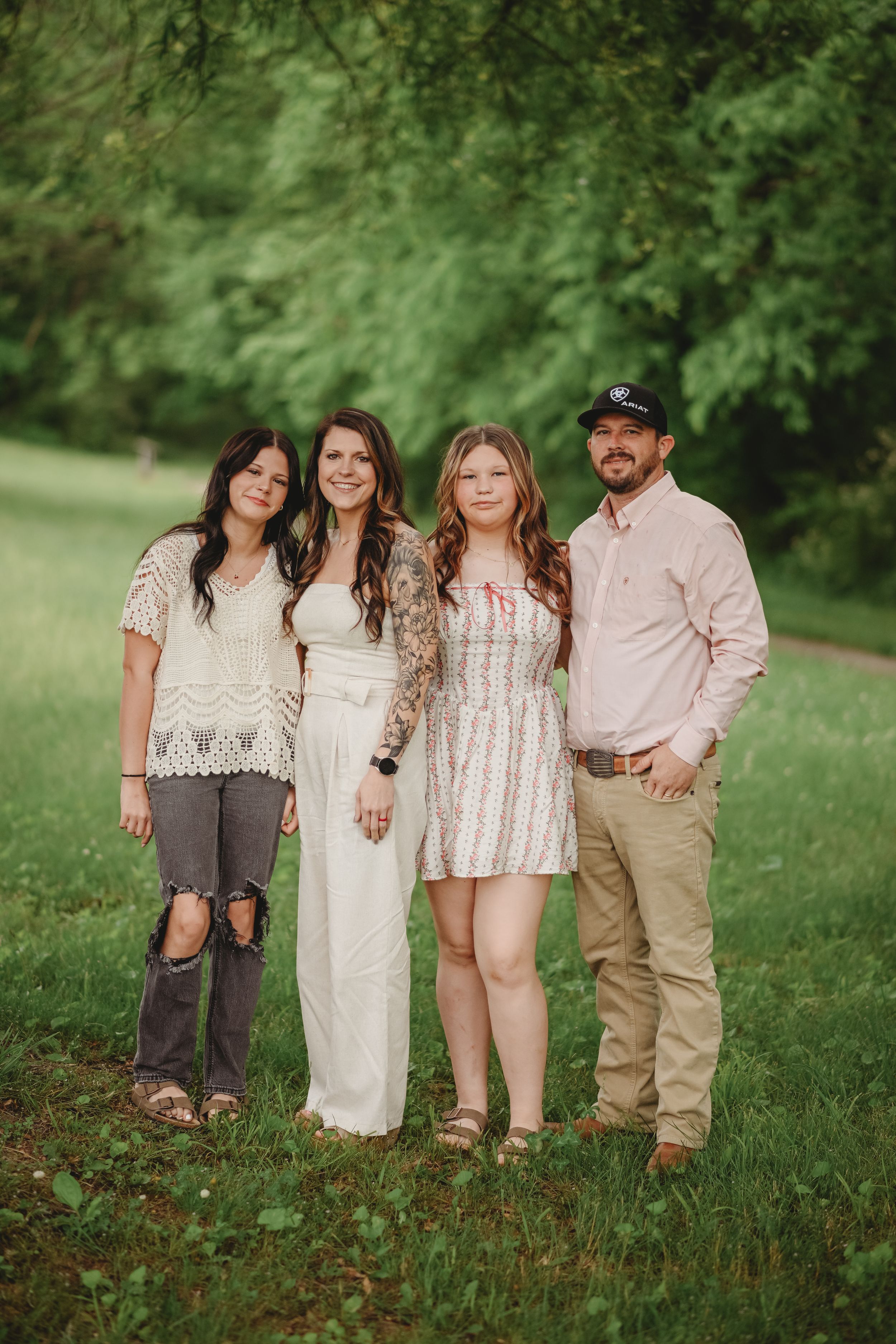 Family group poses together in casual attire against lush green foliage.