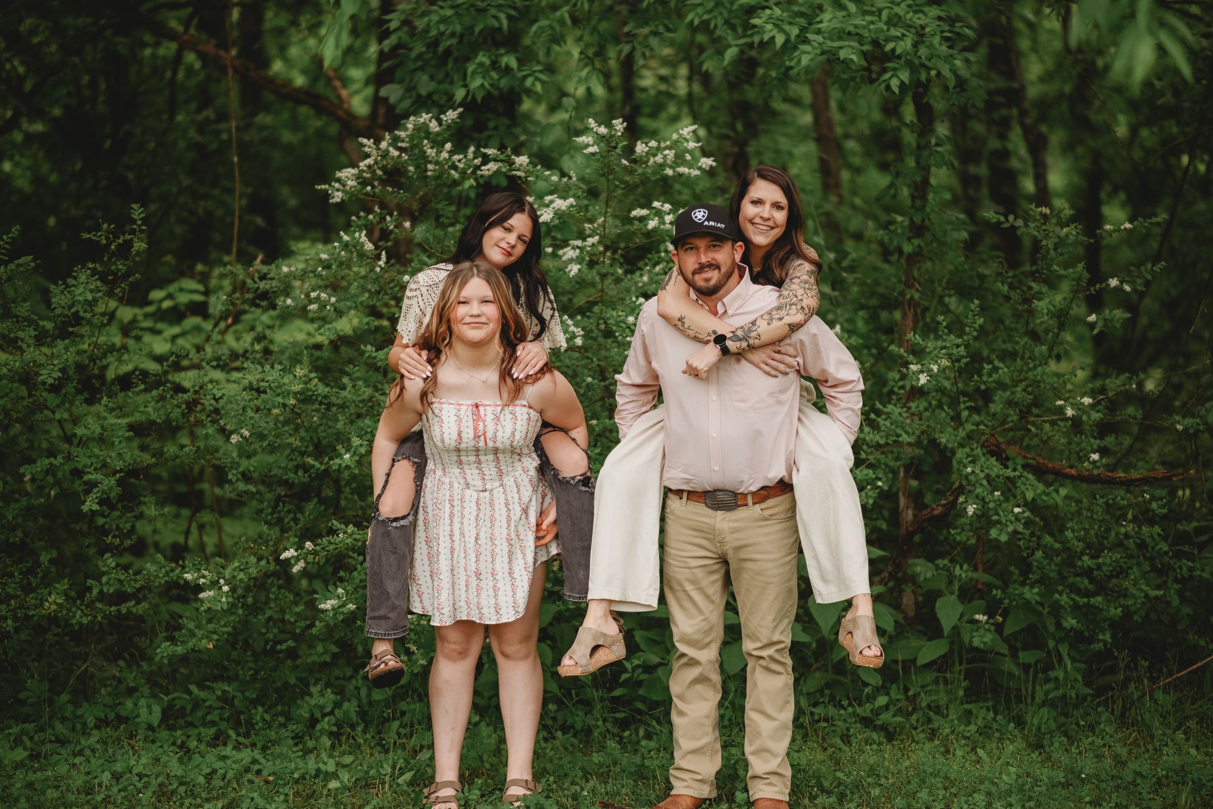 Group portrait in light colored clothing against natural greenery backdrop.