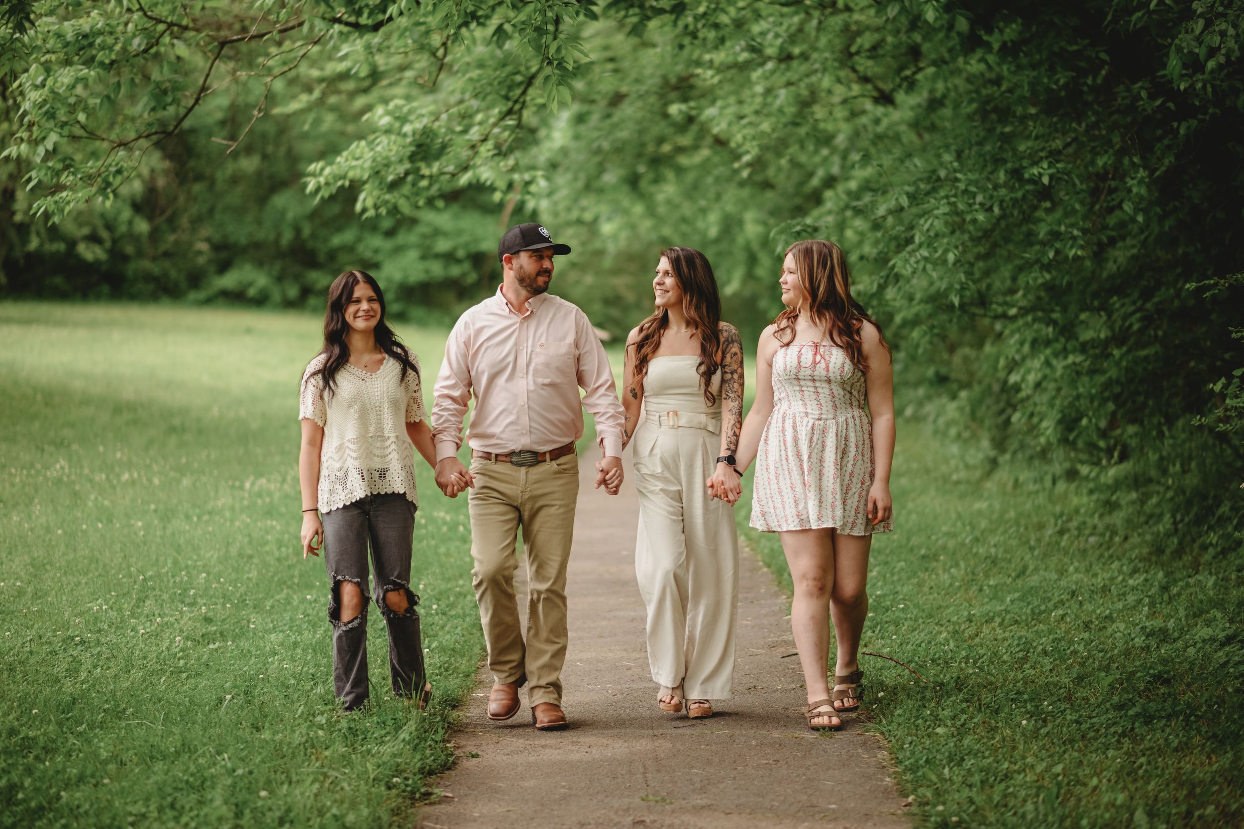 Family walking together on a grassy path surrounded by trees.