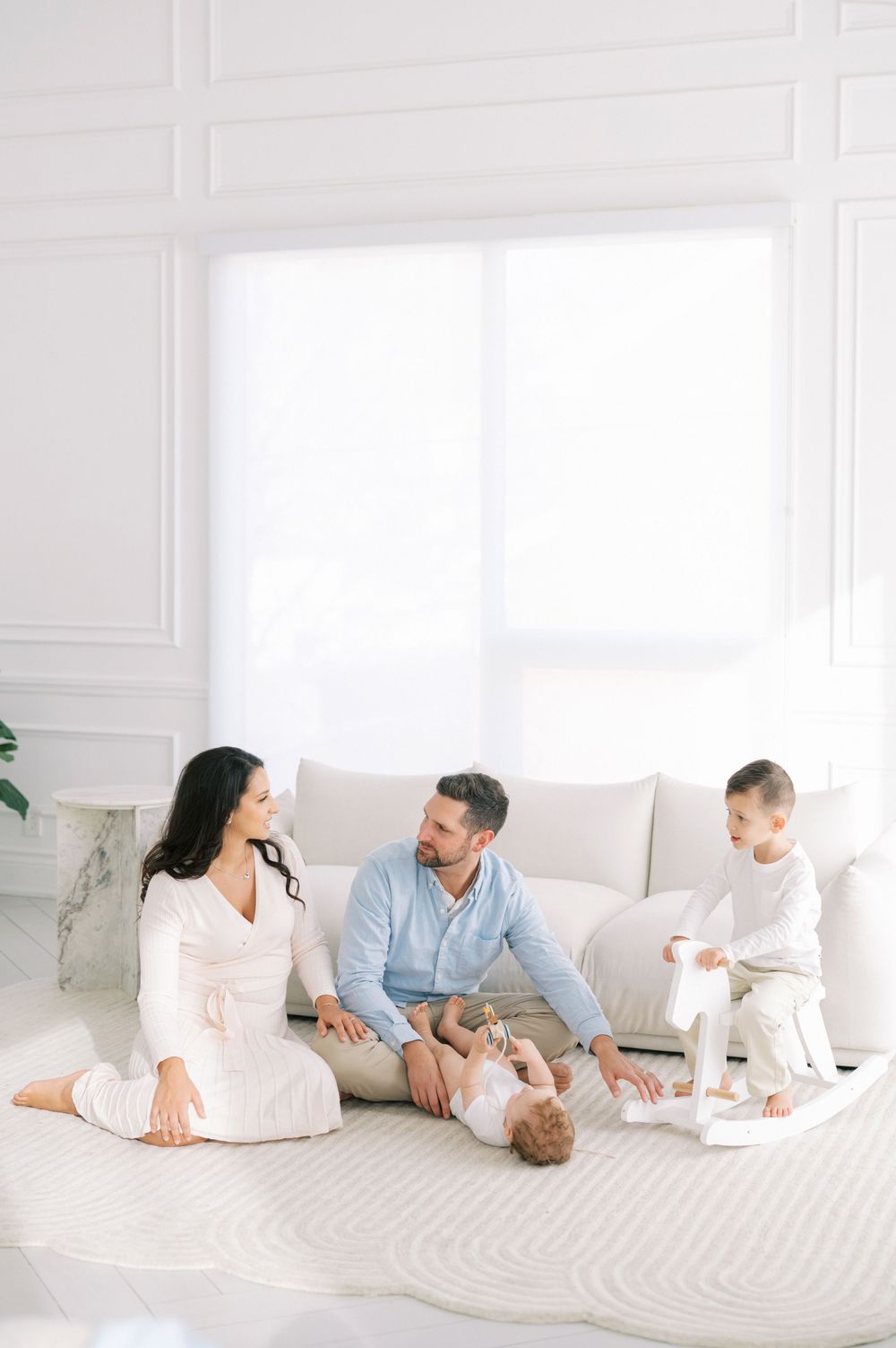 A family relaxes together on a white couch in a bright, minimalist room with white decor.