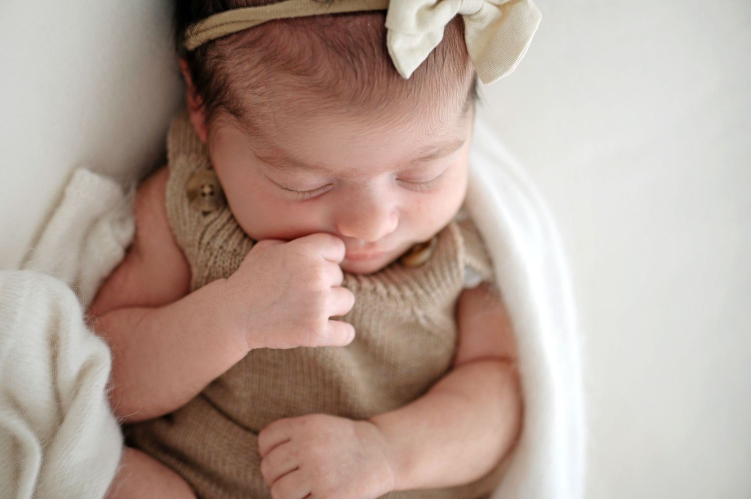 Baby wearing hooded animal outfit being held in soft natural lighting.