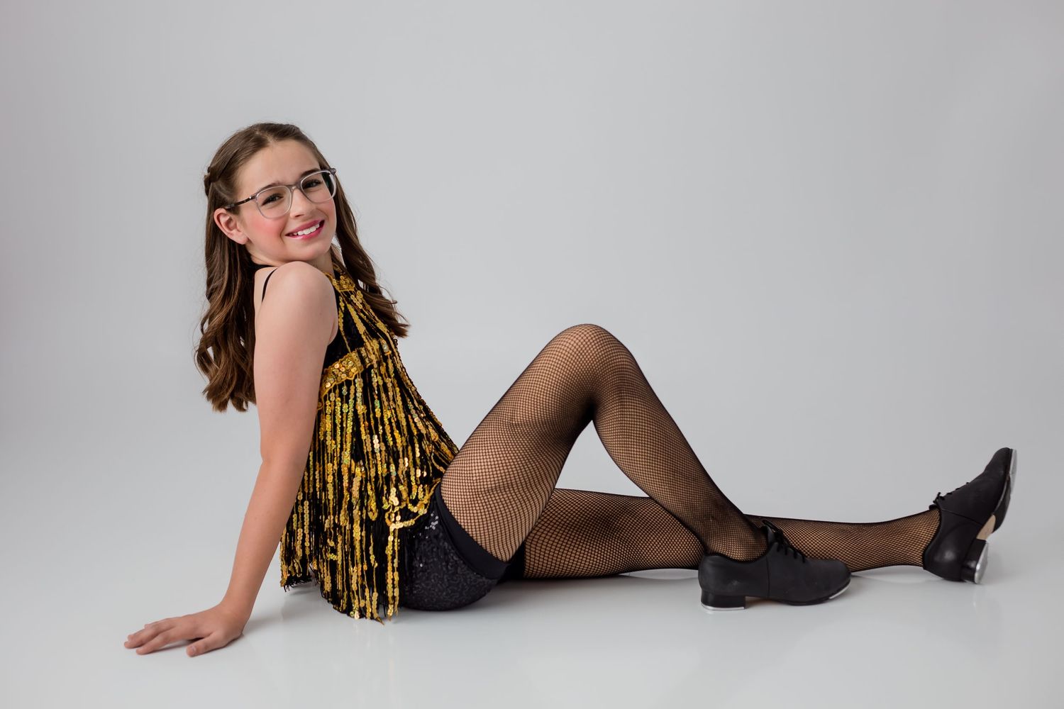 A posed dance portrait of a child dressed in a black & yellow flapper costume for tap dance, against a solid white background.