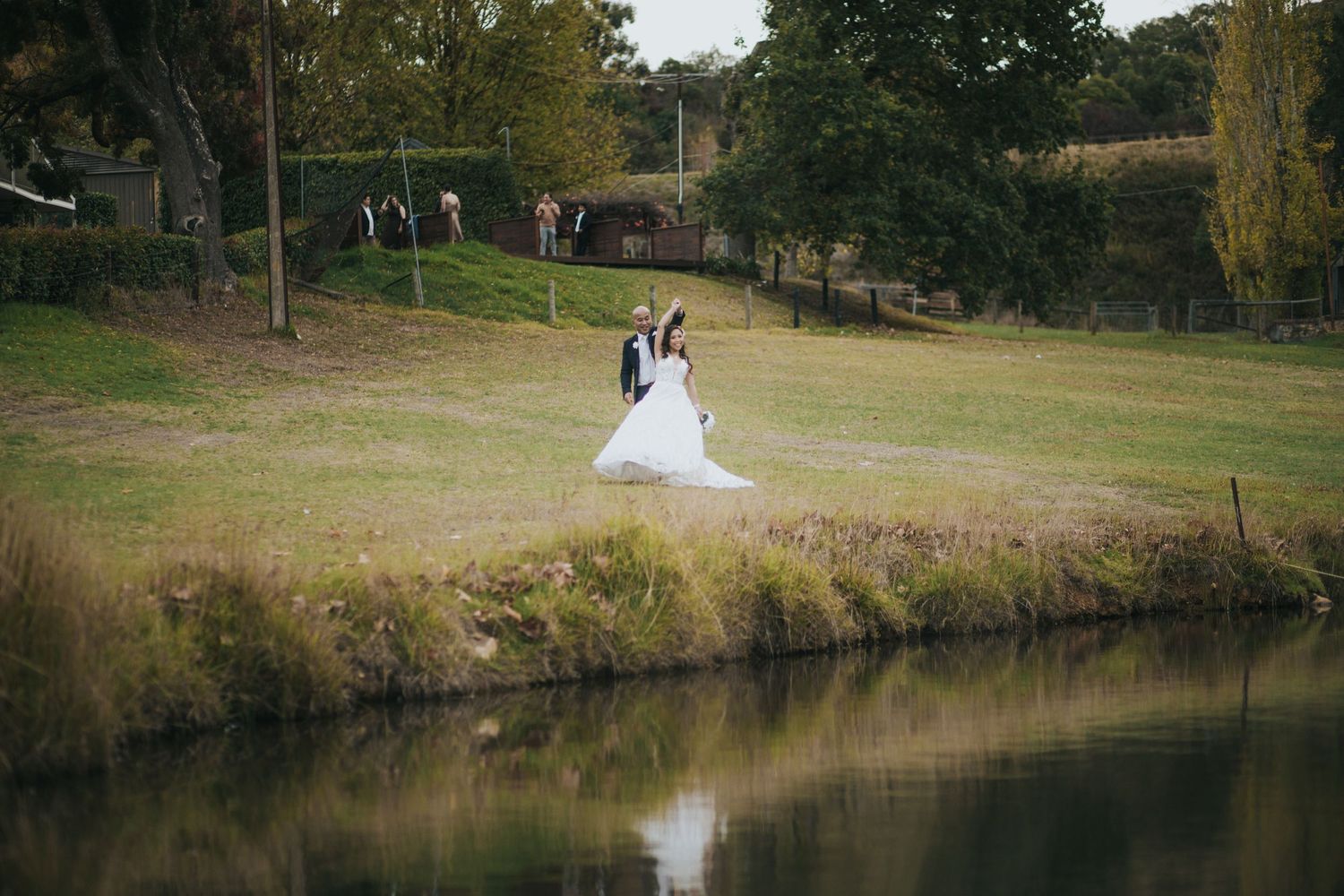 Bride and groom share romantic moment beside tranquil pond in vast open countryside wedding setting.