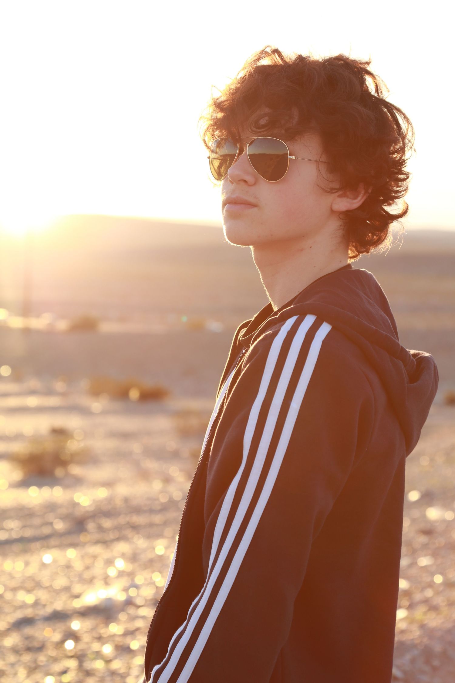 Silhouetted figure in Adidas track jacket against golden sunset light on beach. boy senior pic, sunset california